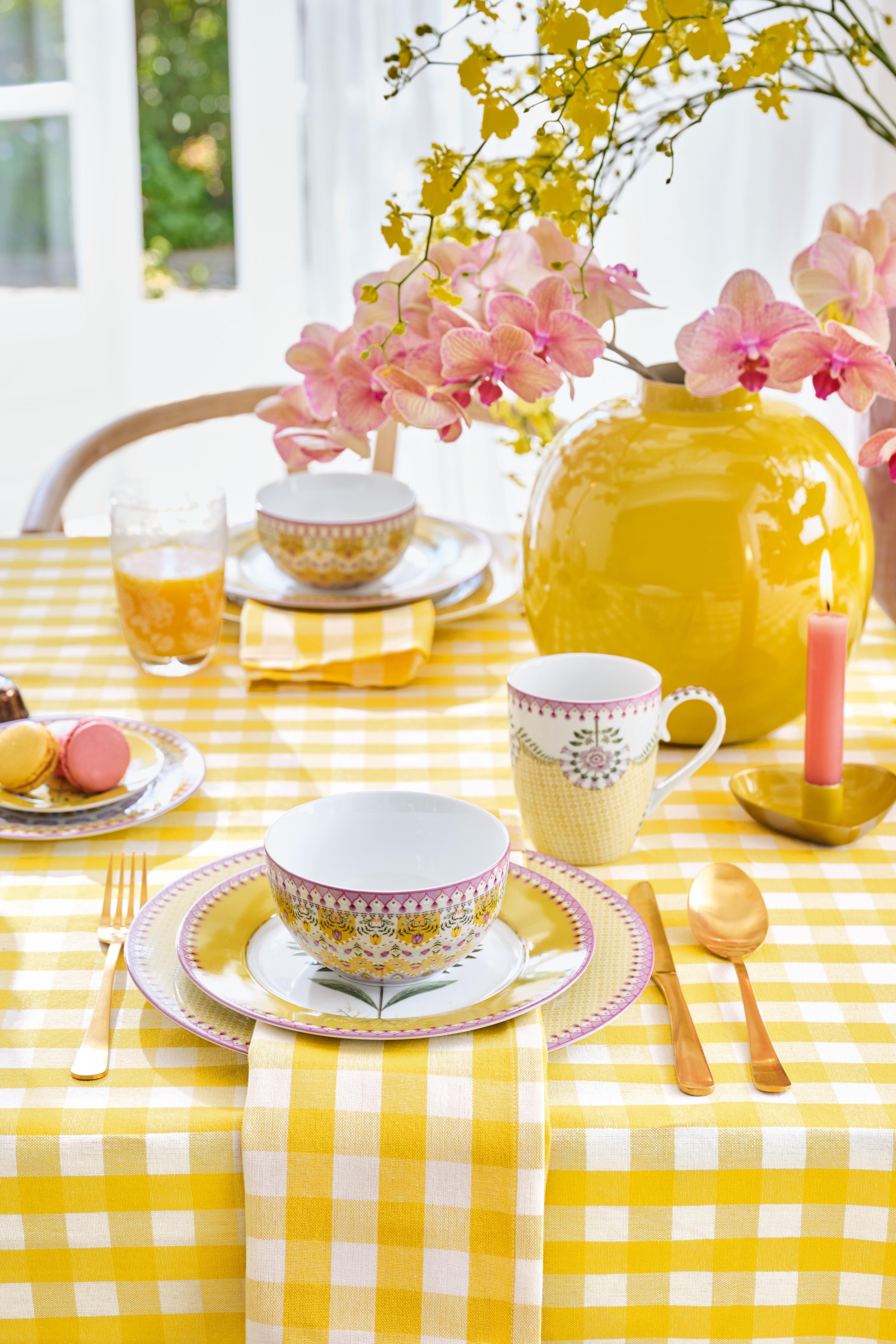 Slavnostně prostřený jídelní stůl se žlutým kostkovaným textilem, porcelánem Pip Studio Lily & Lotus Yellow a kulatou žlutou kovovou vázou.